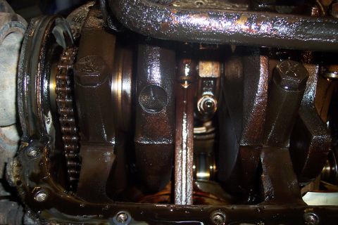 1995 Ford Bronco - A close-up view of the internal engine components, including the crankshaft, connecting rods, and timing chain, all heavily coated in oil.