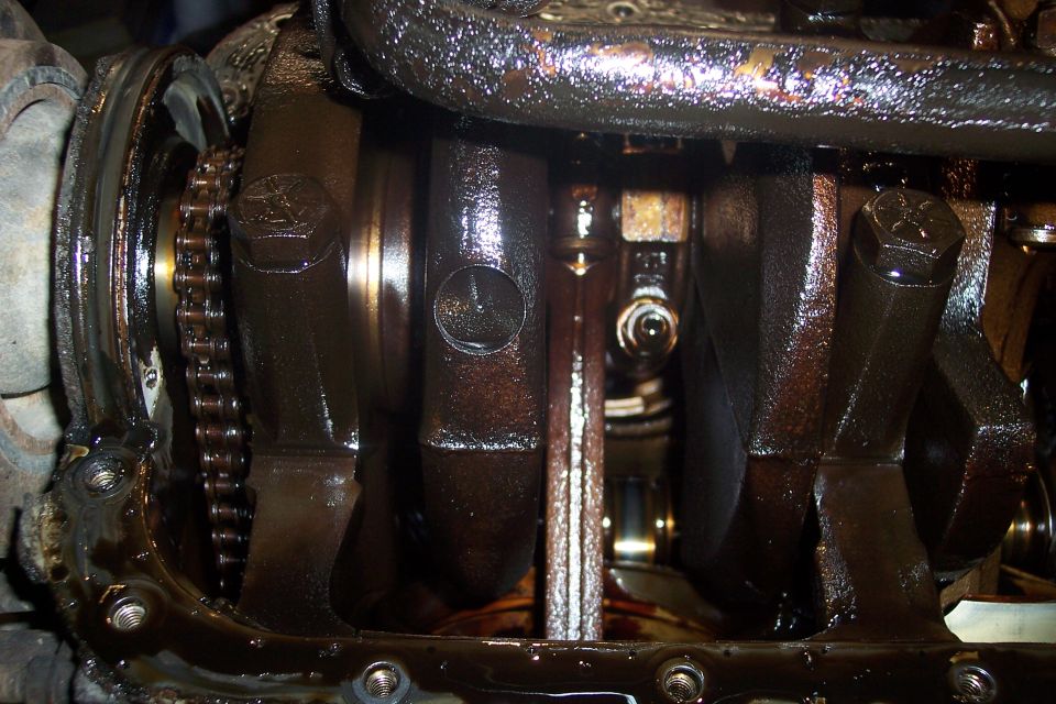 Close-up of engine crankshaft, connecting rods, and timing chain covered in oil.
