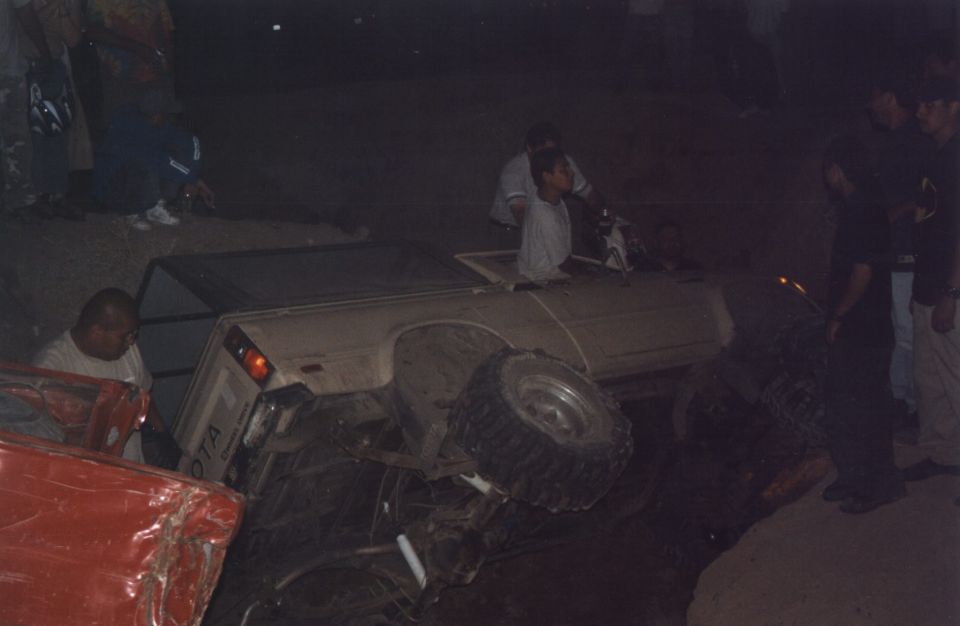Overturned Toyota pickup truck on its side, with people gathered around