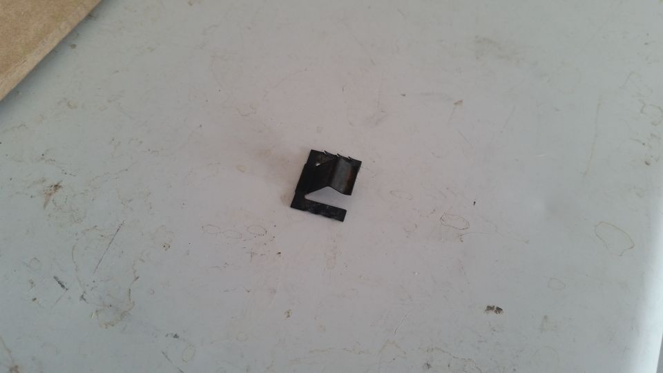 Black metal clip with three prongs on a textured white surface