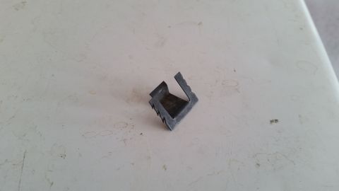 1985 Ford Bronco - A small, dark gray, L-shaped metal bracket with serrated edges is shown on a speckled white surface.