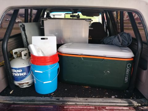 1996 Ford Bronco - The cargo area of a vehicle is filled with camping and cooking equipment, including a propane tank, buckets, a cooler, and a metal containe…