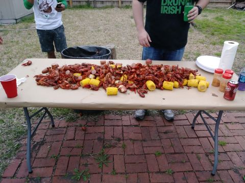 1996 Ford Bronco - A table is laden with a large pile of crawfish, corn on the cob, and sausage, set up for an outdoor meal. Two people stand behind the table…