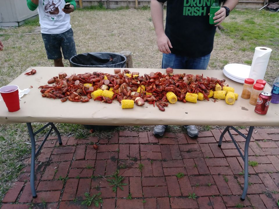 Outdoor crawfish boil with corn and sausage on a table, two people standing behind it.