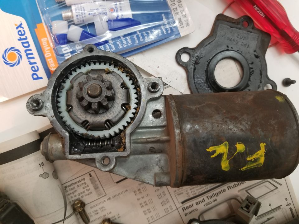 Disassembled power window motor assembly with gears, springs, and motor housing.