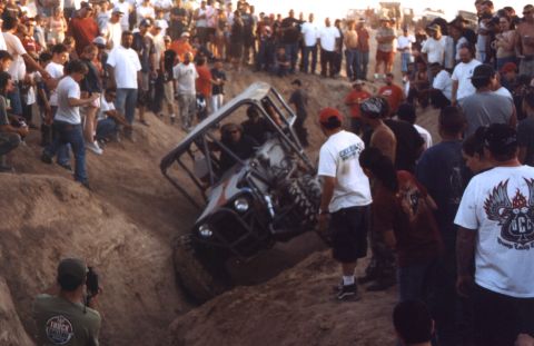 2000 Ford F-450 - An off-road buggy is stuck in a steep dirt ditch while a crowd watches.