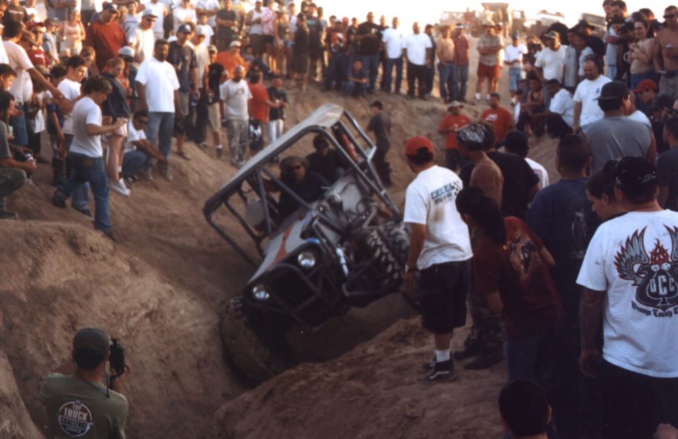 Off-road buggy tilted in a dirt ditch, surrounded by onlookers
