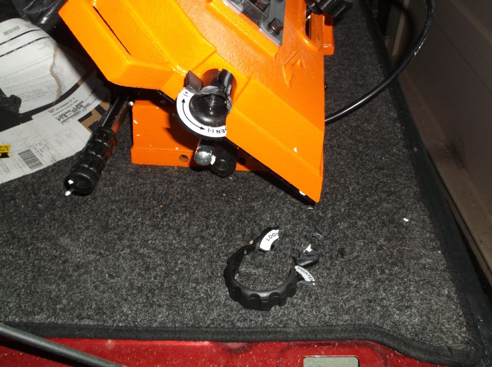Broken black plastic knob with "LOOSEN" and "TIGHTEN" text on gray carpet next to orange tool.
