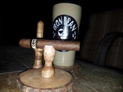 2018 Ford Bronco - A cigar rests on a wooden stand in front of a tumbler with a "Iron Bean" sticker. The scene is set on an outdoor table at night.
