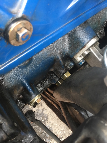 1981 Ford Bronco - A close-up view of engine components, including a blue painted valve cover, a black cast iron manifold, and various bolts and hoses. The im…