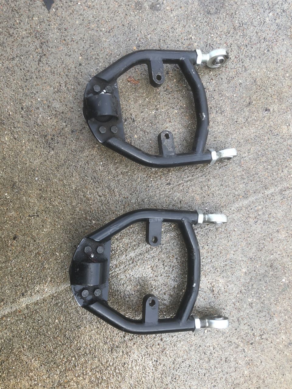 Pair of black tubular control arms with rod ends on wet concrete