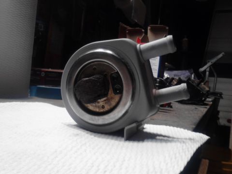 1995 Ford Bronco - A gray automotive part, possibly an oil cooler or filter housing, is shown resting on a white textured surface. The part has two hose fitti…