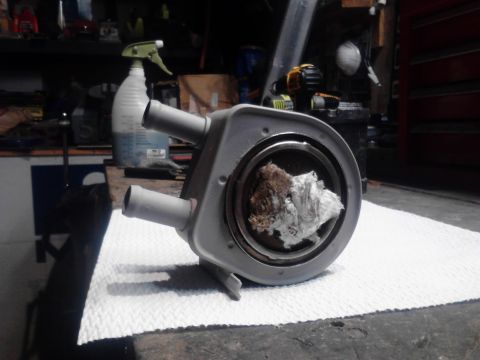 1995 Ford Bronco - A close-up view of a dirty, gray automotive part with two hose connections and debris inside the central opening. The part is resting on a…