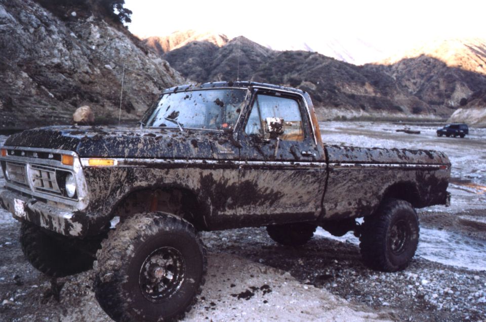 Mud-covered lifted Ford pickup on big tires parked in a rocky canyon at dusk