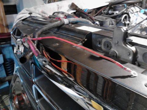 1995 Ford Bronco - Close-up view of red battery cables and wiring harness connected to the front of a black vehicle, possibly a Ford Bronco, with the hood ope…