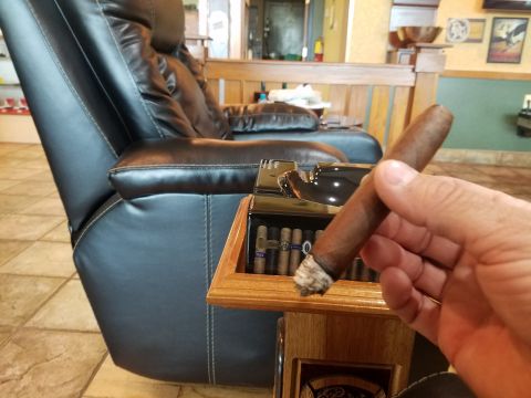 2018 Ford Bronco - A person is holding a lit cigar in their hand, with a cigar humidor and a leather recliner visible in the background.