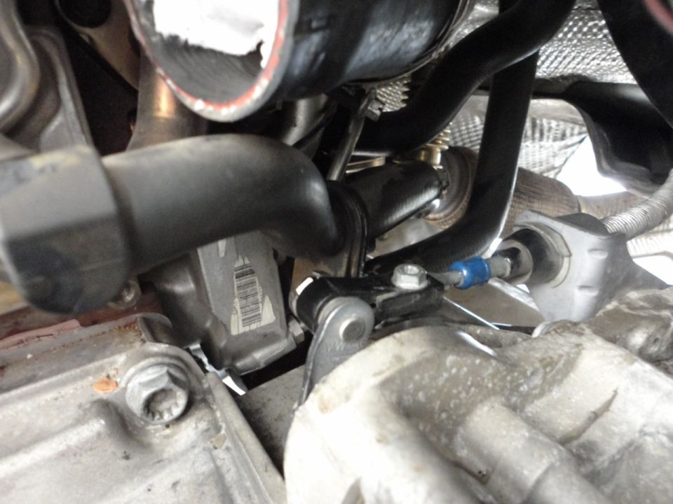 Vehicle engine bay with turbocharger and plumbing, showing black hose with red stripe and blue fitting.