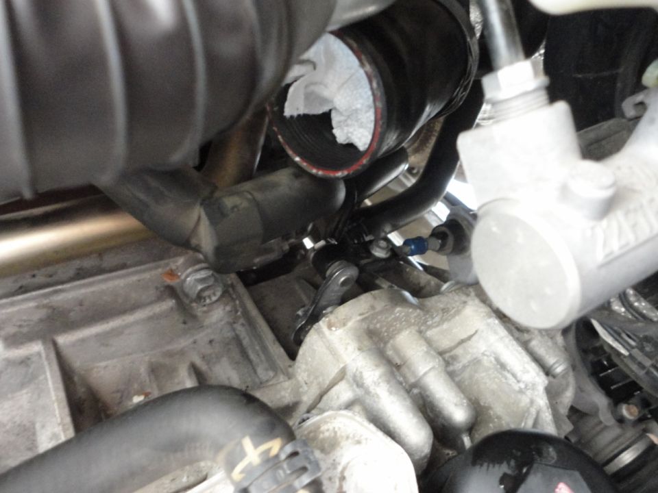 Vehicle engine bay with hoses, metal parts, and a white cloth in a hose.