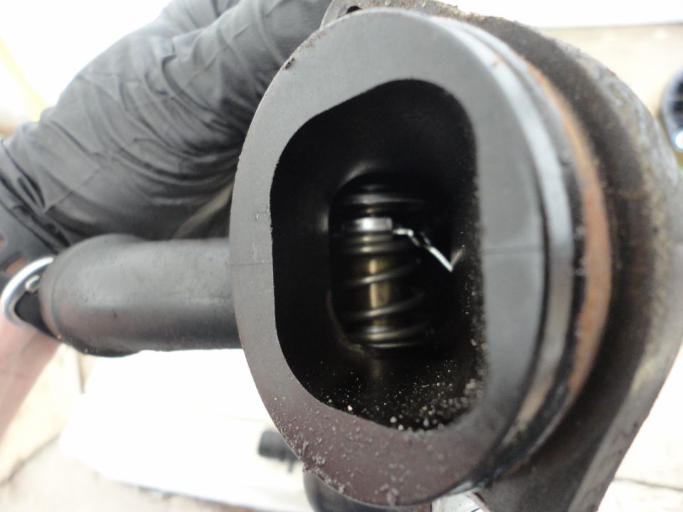 Close-up of a black spring inside a dark housing, held by a gloved hand.