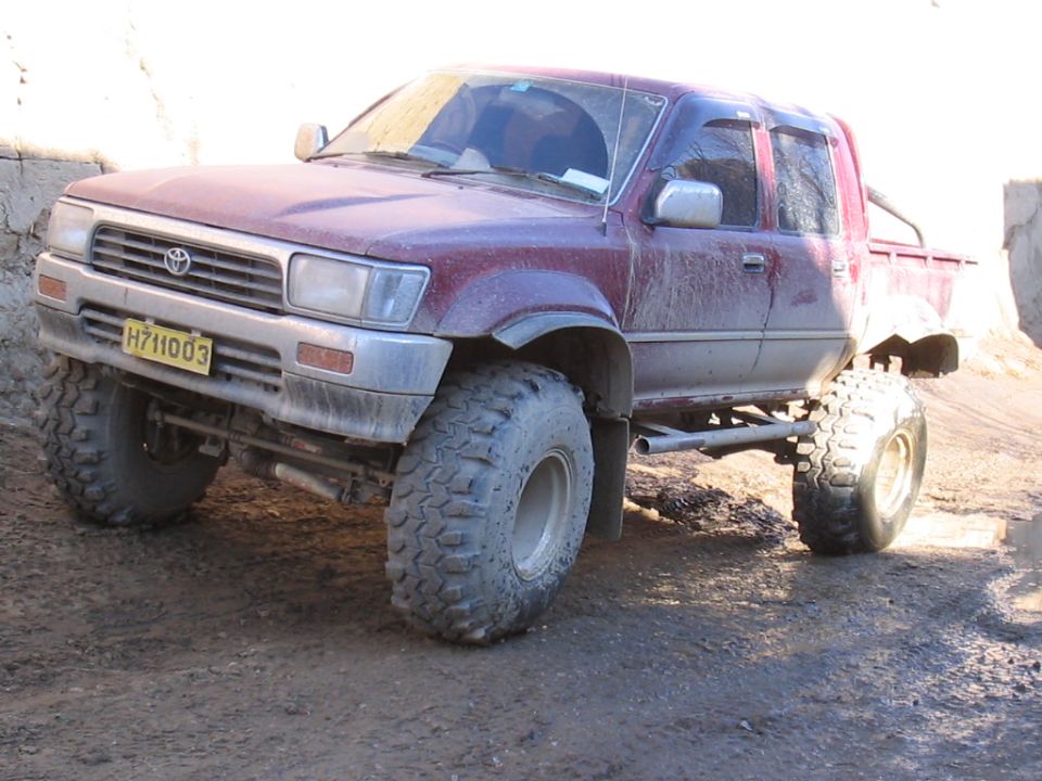 Maroon Toyota pickup truck with large off-road tires and lifted suspension
