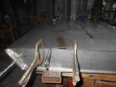 1992 Ford Bronco - Two locking C-clamps are holding down a large, flat piece of sheet metal that is bent at an angle. The sheet metal is resting on a wooden w…