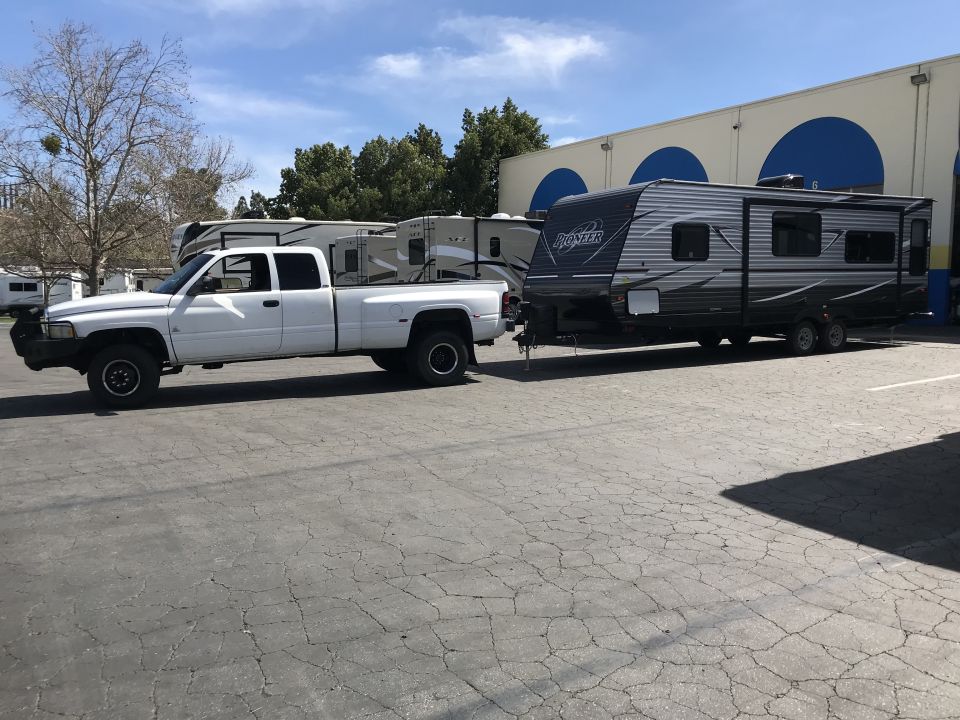 White dually pickup truck towing a Pioneer travel trailer.