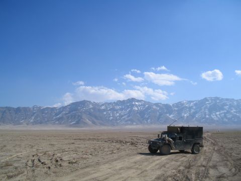 1981 Ford Bronco - A military vehicle sits on a dirt track in a dry, barren landscape under a bright blue sky.