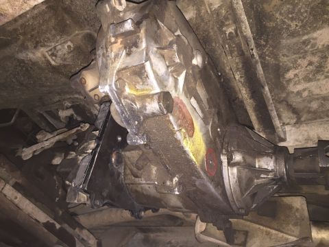 1984 Ford Bronco - The underside of a vehicle shows a transfer case assembly, likely from a 1984 Ford Bronco, with visible grease and dirt accumulation. The t…