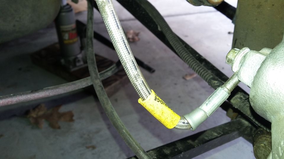 Braided high-pressure hose with yellow tag connected to a fitting on a vehicle