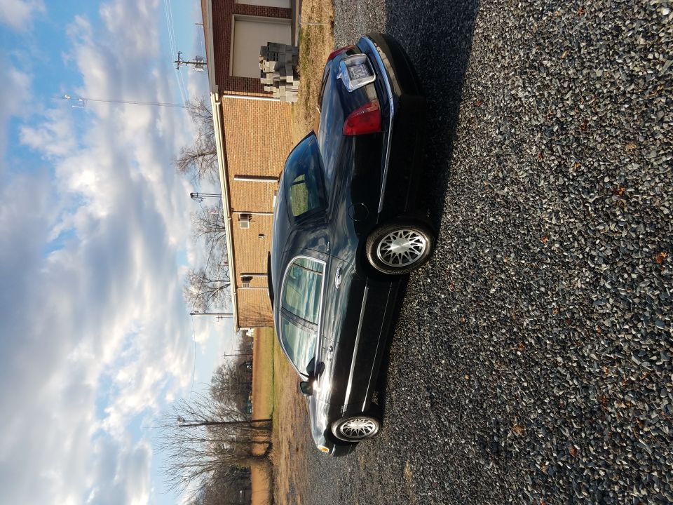 Black 2002 Lincoln Town Car parked on gravel lot.