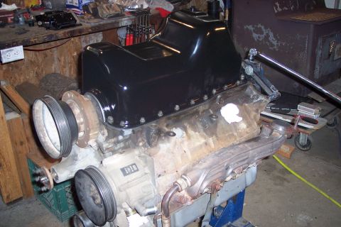 1995 Ford Bronco - A black oil pan is bolted onto the top of a V8 engine block, which is mounted on an engine stand. The engine has several pulleys and access…