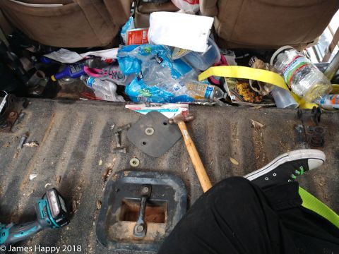 1989 Ford Bronco - The interior of a vehicle is filled with trash and tools, including a hammer, a power drill, and various plastic bottles and bags. A person…