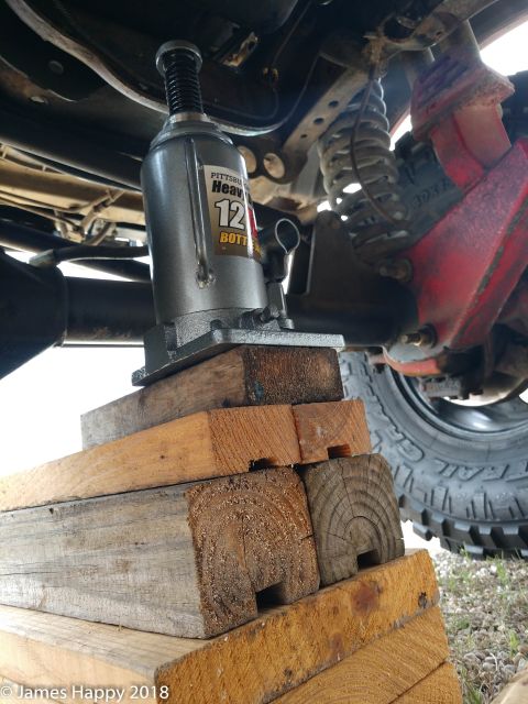1989 Ford Bronco - A bottle jack is used to lift a vehicle, supported by stacked wooden blocks for safety.