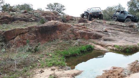1995 Ford Bronco - Two off-road vehicles, a 1995 Ford Bronco and a Jeep, navigate a rocky incline.