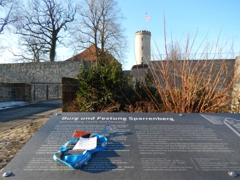 2010 Audi A4 - A sign detailing Sparrenberg Castle and Fortress stands in front of the castle's tower and walls under a clear blue sky.
