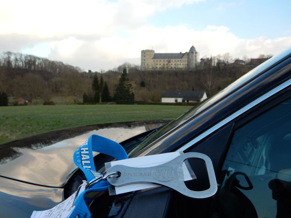 Car hood with blue tow strap and metal bottle opener keychain. Castle in background