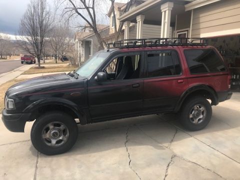 2000 Ford Explorer - Side view of a two-tone 2000 Ford Explorer SUV equipped with a roof rack, parked on a driveway.
