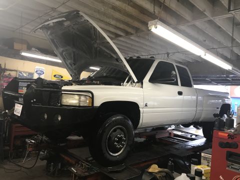1997 Dodge 3500 - A white dually pickup truck is being worked on in a garage with its hood open.