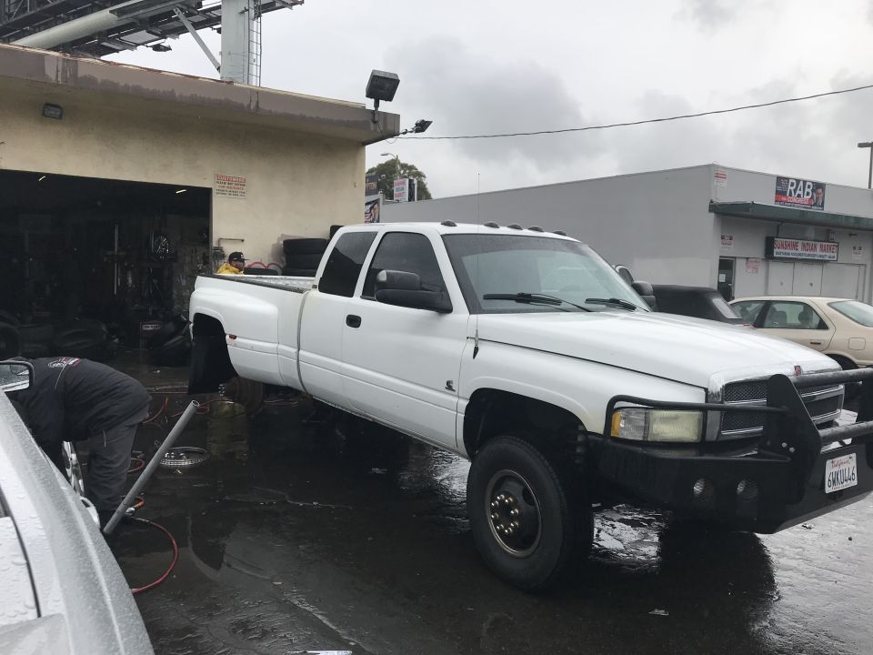 1997 Dodge 3500 dually pickup truck parked outside a garage with a man working on the front wheel