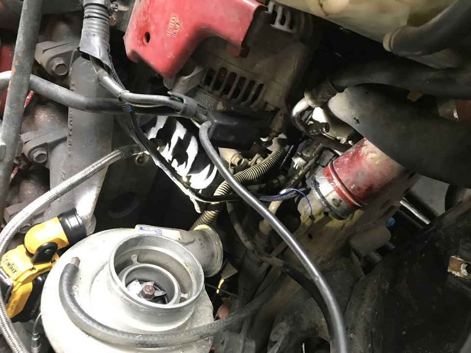 Engine bay close-up showing exposed turbocharger compressor wheel, alternator, hoses and wiring on a diesel truck