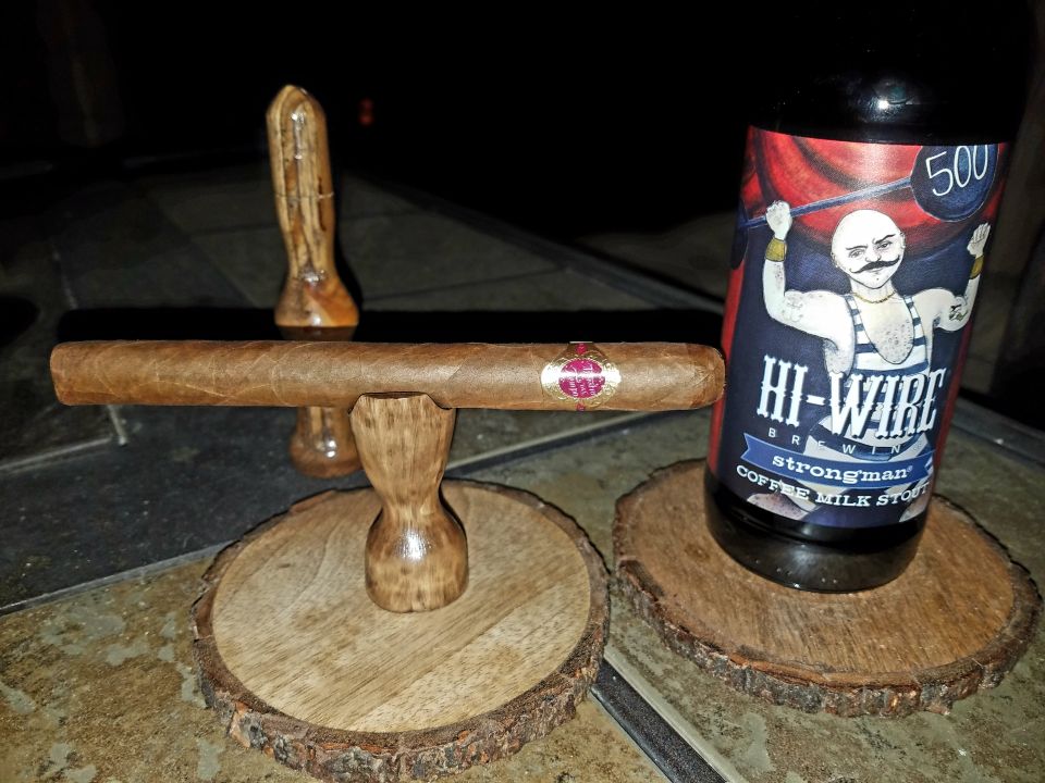 Cigar resting on wooden stand next to a bottle of Hi-Wire Brewing coffee milk stout