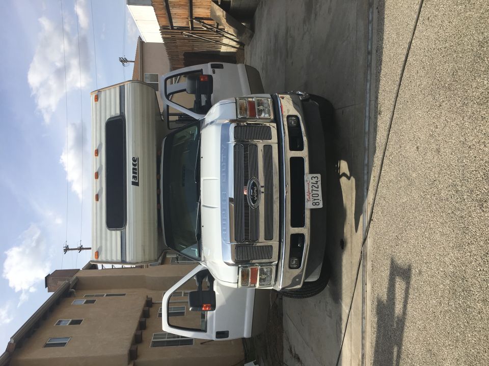 White Ford F-Series truck with a Lance camper, front view, driver's door open, California license plate 8Y07243
