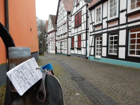 2010 Audi A4 - A close-up of a note attached to a metal post on a street lined with traditional European houses.