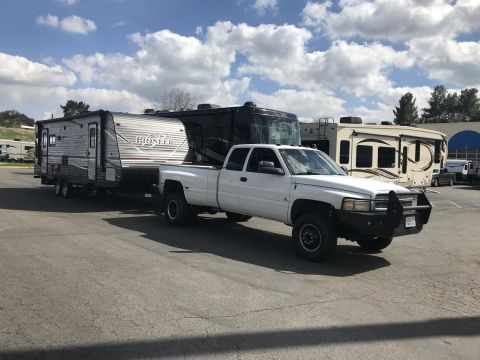 2018 Yugo GV - A white pickup truck is parked with a travel trailer hitched to it, alongside other recreational vehicles.
