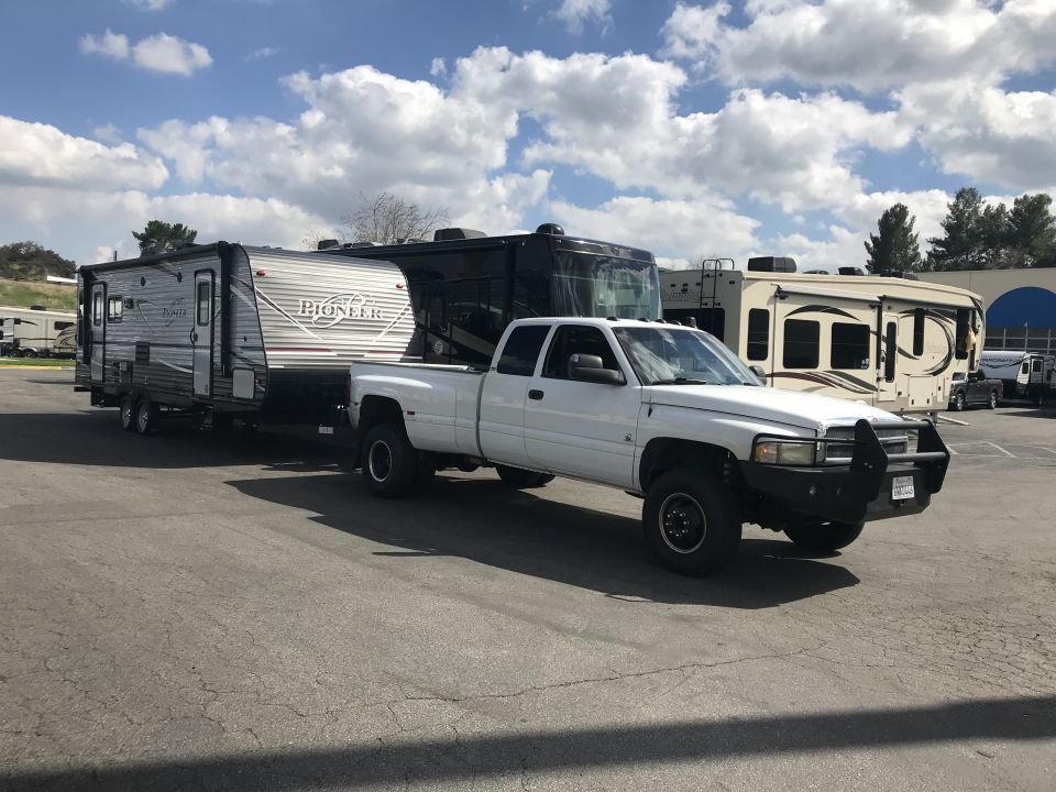 White pickup truck towing a travel trailer, with other RVs in the background