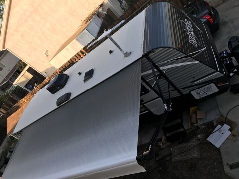 2018 Yugo GV - A recreational vehicle is parked in a driveway with its awning extended, alongside a dark-colored car.
