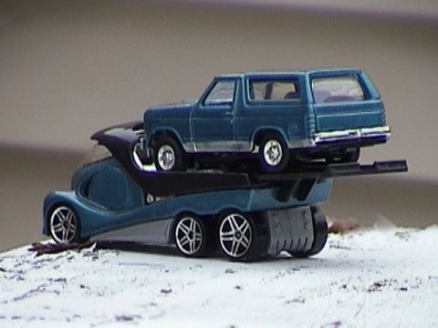 1979 Ford Bronco - A blue 1979 Ford Bronco is loaded onto a tow truck, with both vehicles appearing to be toy models.