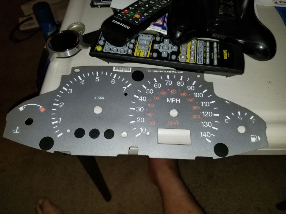 Bare speedometer instrument cluster faceplate with MPH and km/h markings on table