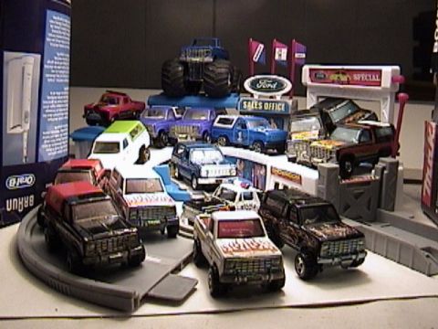 1979 Ford Bronco - A collection of toy trucks and SUVs, including several Ford Bronco models, are displayed in a simulated dealership environment.