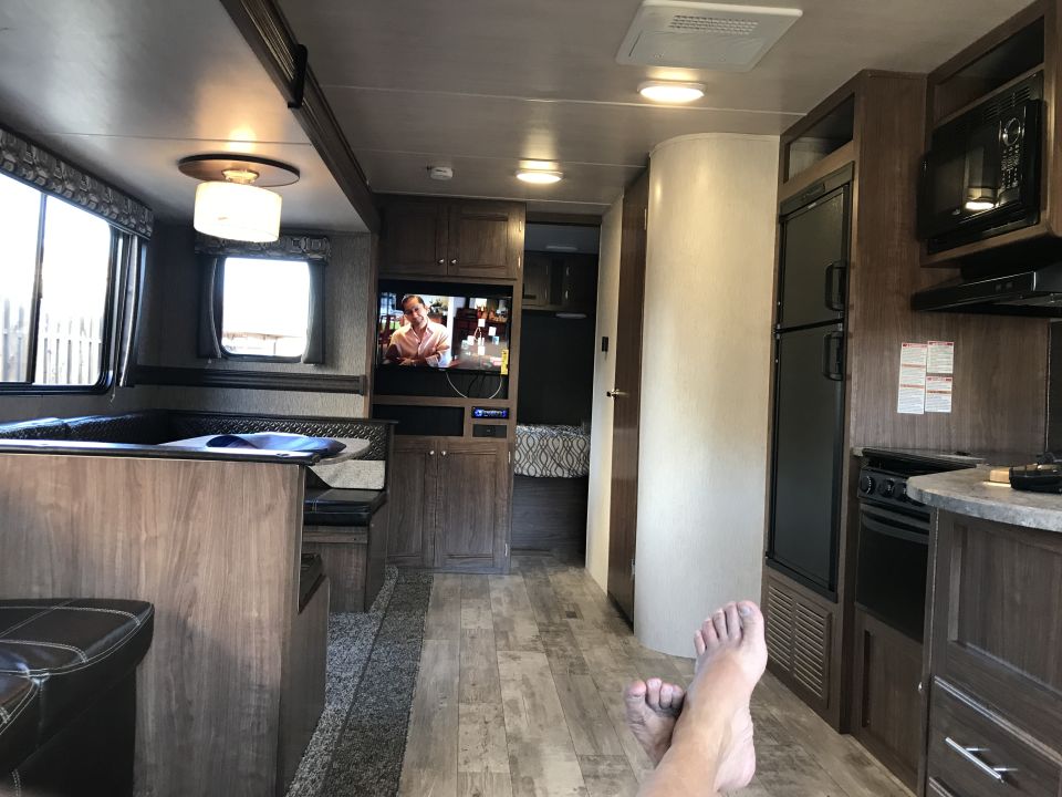 RV interior with a couch, TV, kitchen area, and feet resting on the floor